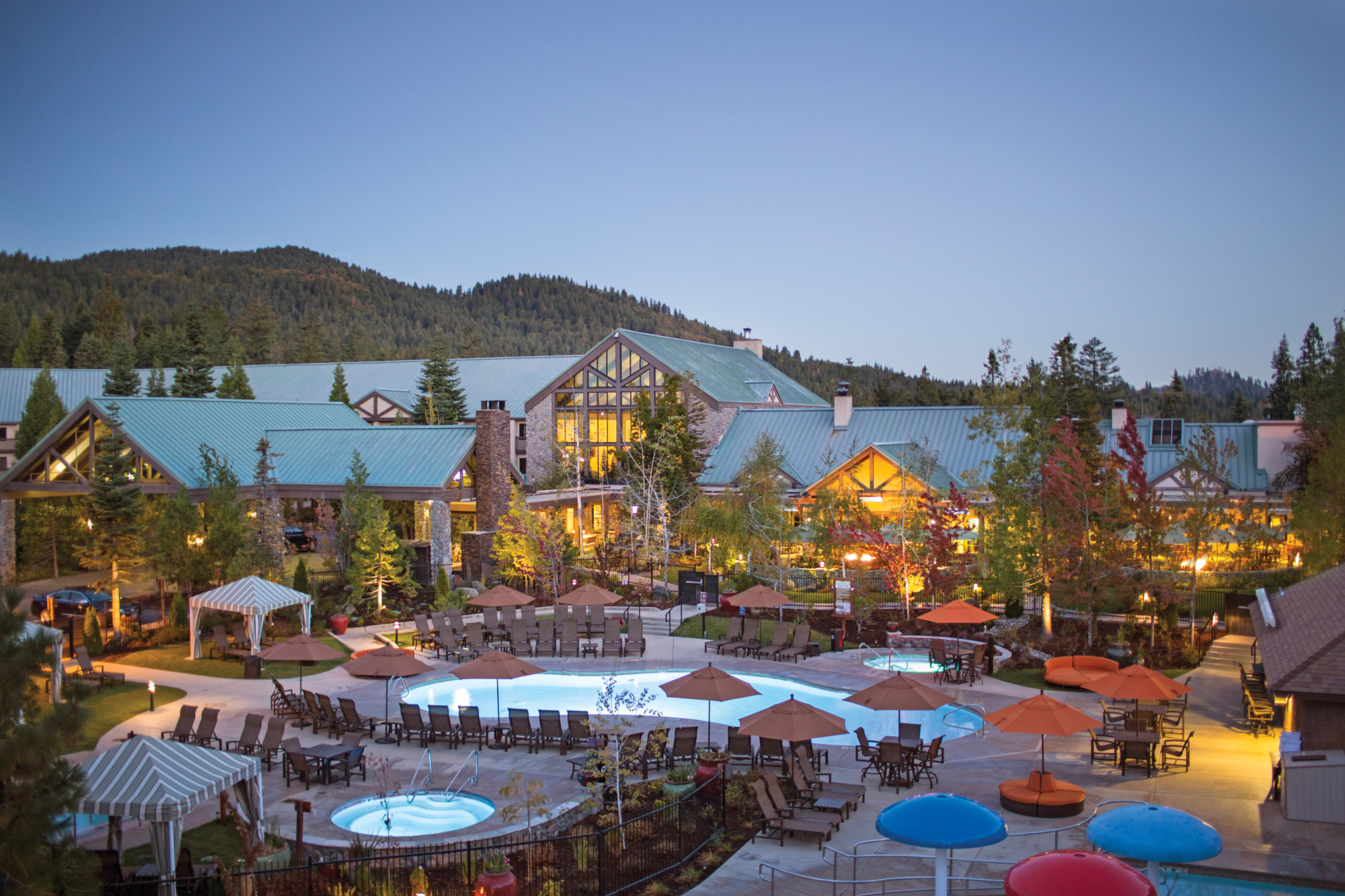 The Tenaya resort with a pool surrounded by umbrellas at dusk.