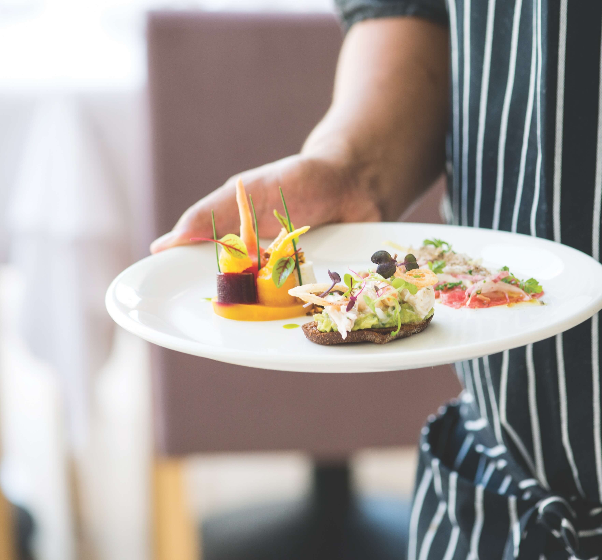 A waiter holding a white plate with a variety of delicate foods.