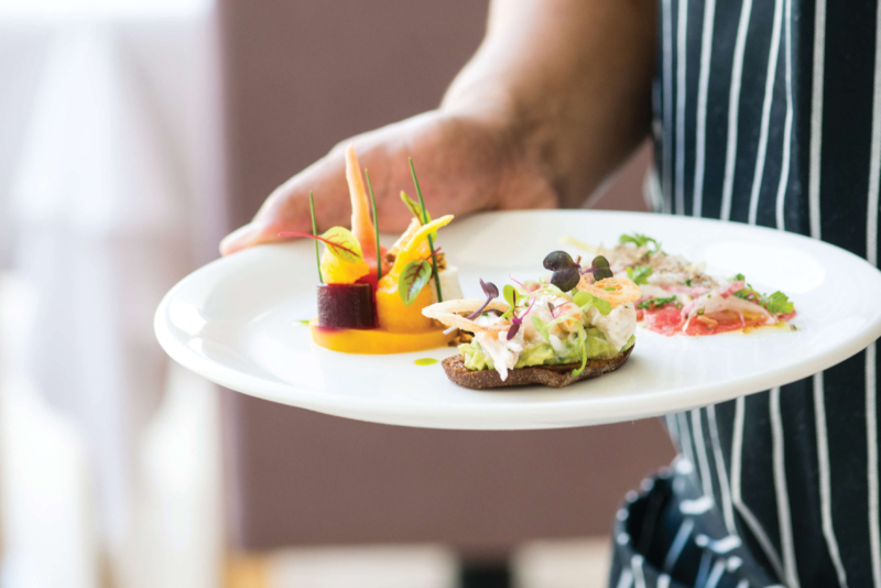 A waiter holding a white plate with a variety of delicate foods.