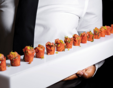 A person holding a long white tray with appetizers on it.