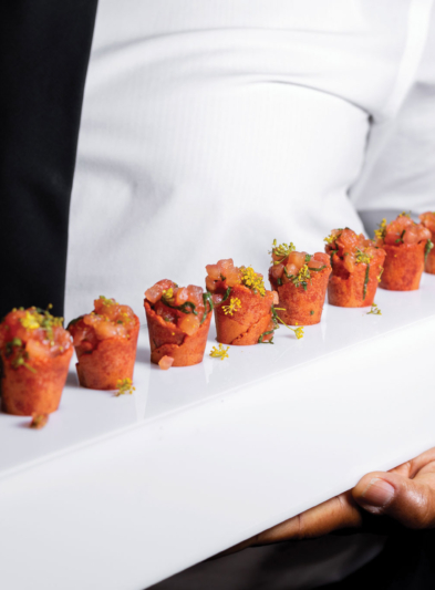 A person holding a long white tray with appetizers on it.