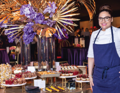 A smiling chef standing in front of a table at Emmy's filled with desserts.