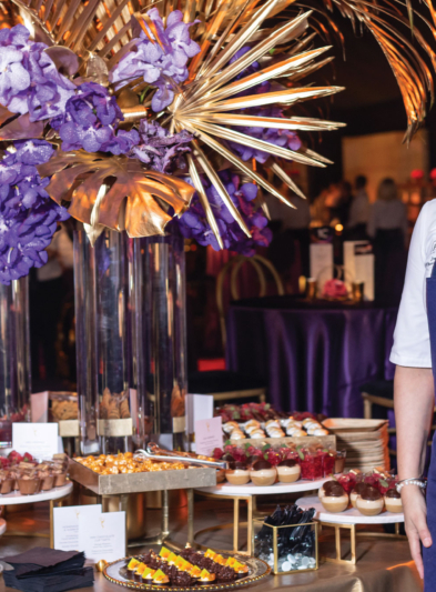 A smiling chef standing in front of a table at Emmy's filled with desserts.
