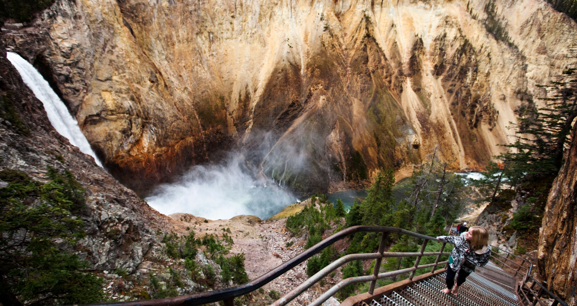 A person walking up a steel staircase next to a waterfall at Yellowstone.