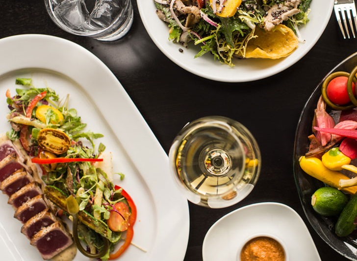 A table at Patina 250 topped with plates of food and a glass of white wine.